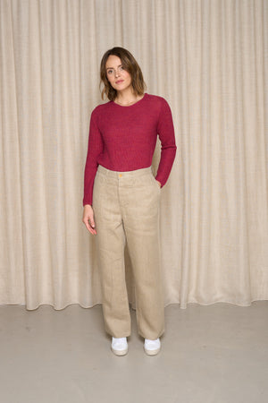Femme portant le jeans en chanvre Belna en Chanvre Naturel, de couleur naturelle avec coupe large et taille haute, accompagné d’un pull rouge et des baskets blanches, sur fond de rideau beige - Le Gaulois jeans