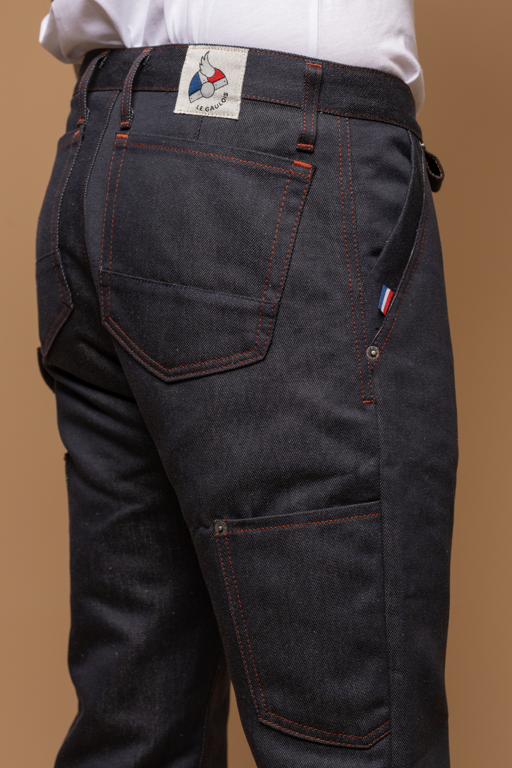 Plan rapproché du jeans en lin et coton bio Cargus à coupe droite cargo et taille mi-haute, de couleur bleu jeans, détail de la poche arrière, de la poche cargo et de l'étiquette de la marque Le Gaulois, avec un t-shirt blanc, sur fond neutre - Le Gaulois jeans