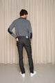 Modèle homme de dos portant le jeans en lin et élasthanne recyclé Divio Noir à coupe près du corps et taille haute, couleur noir jeans, avec un pull à rayures et des baskets blanches, sur fond beige uni - Le Gaulois jeans