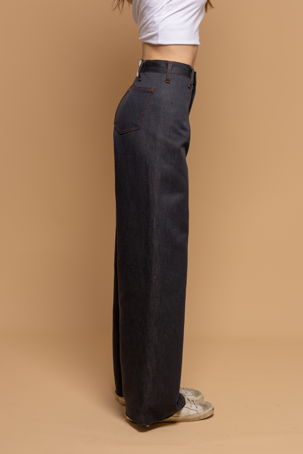 Modèle femme portant le jeans en lin et coton bio Flavia à coupe évasée en bas et taille mi-haute, de couleur bleu jeans, avec un t-shirt blanc et des baskets blanches, sur fond neutre - Le Gaulois jeans
