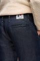 Jeans en lin Lugdunum Bleu pour homme avec coupe chino, taille haute confortable et légèrement effilé aux chevilles, couleur bleu jeans, détail de l'étiquette Le Gaulois sur la poche arrière, porté sous un pull beige, fabriqué en France - Le Gaulois jeans