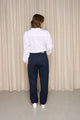 Modèle féminin de dos portant le jeans en lin Lutèce Bleu à coupe Mom, taille haute, couleur bleu marine, associé à une chemise blanche, sur fond beige - Le Gaulois Jeans