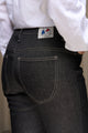 Modèle femme portant le jeans en lin et élasthanne recyclé Nicia Noir à coupe près du corps et taille haute, fermeture à glissière, sur fond de mur clair, mettant en avant le tissu sergé croisé et le label Le Gaulois jeans sur la poche arrière.