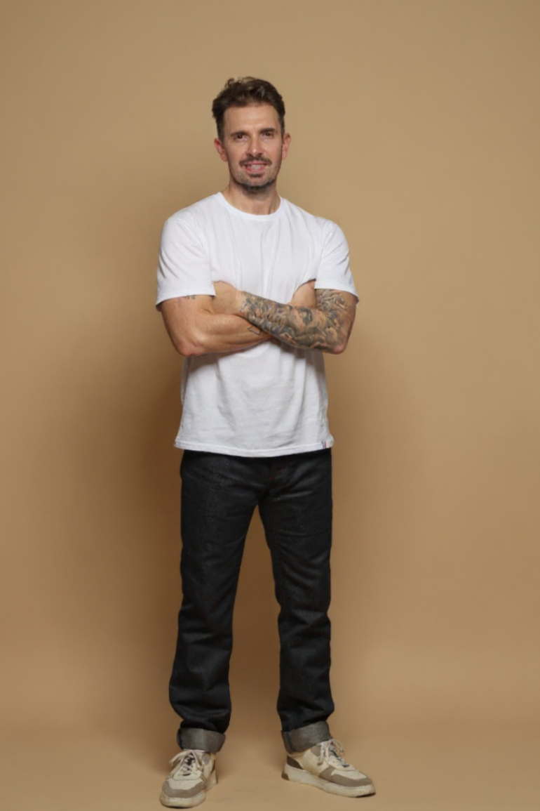 Modèle homme portant le jeans en lin et coton bio Ruscino à coupe droite et taille mi-haute, de couleur bleu jeans, avec un t-shirt blanc et des baskets beiges, sur fond neutre - Le Gaulois jeans