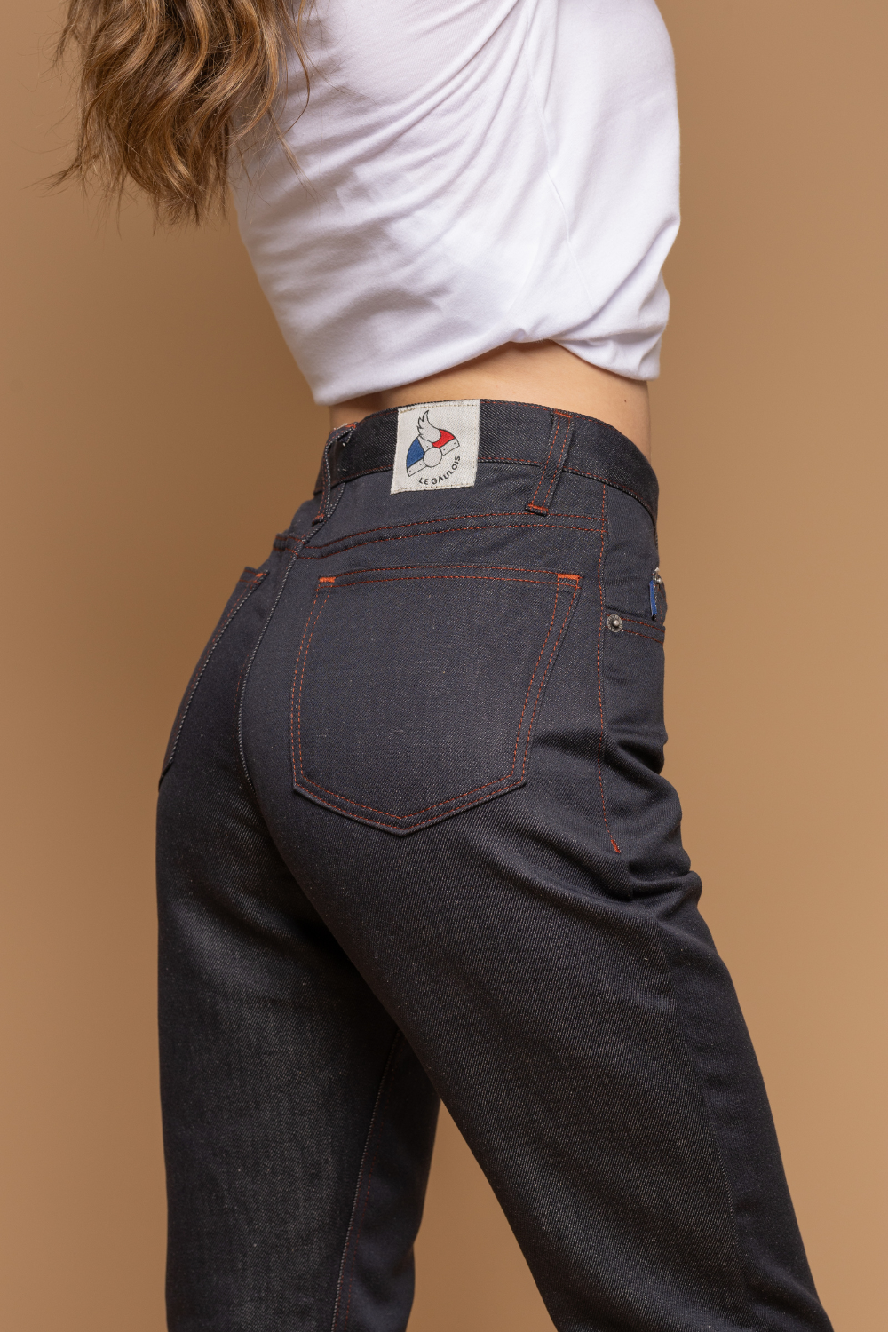 Plan rapproché du jeans en lin et coton bio Tarba à coupe droite et taille mi-haute, de couleur bleu jeans, détail de la poche arrière et étiquette de la marque Le Gaulois, avec un t-shirt blanc, sur fond neutre - Le Gaulois jeans