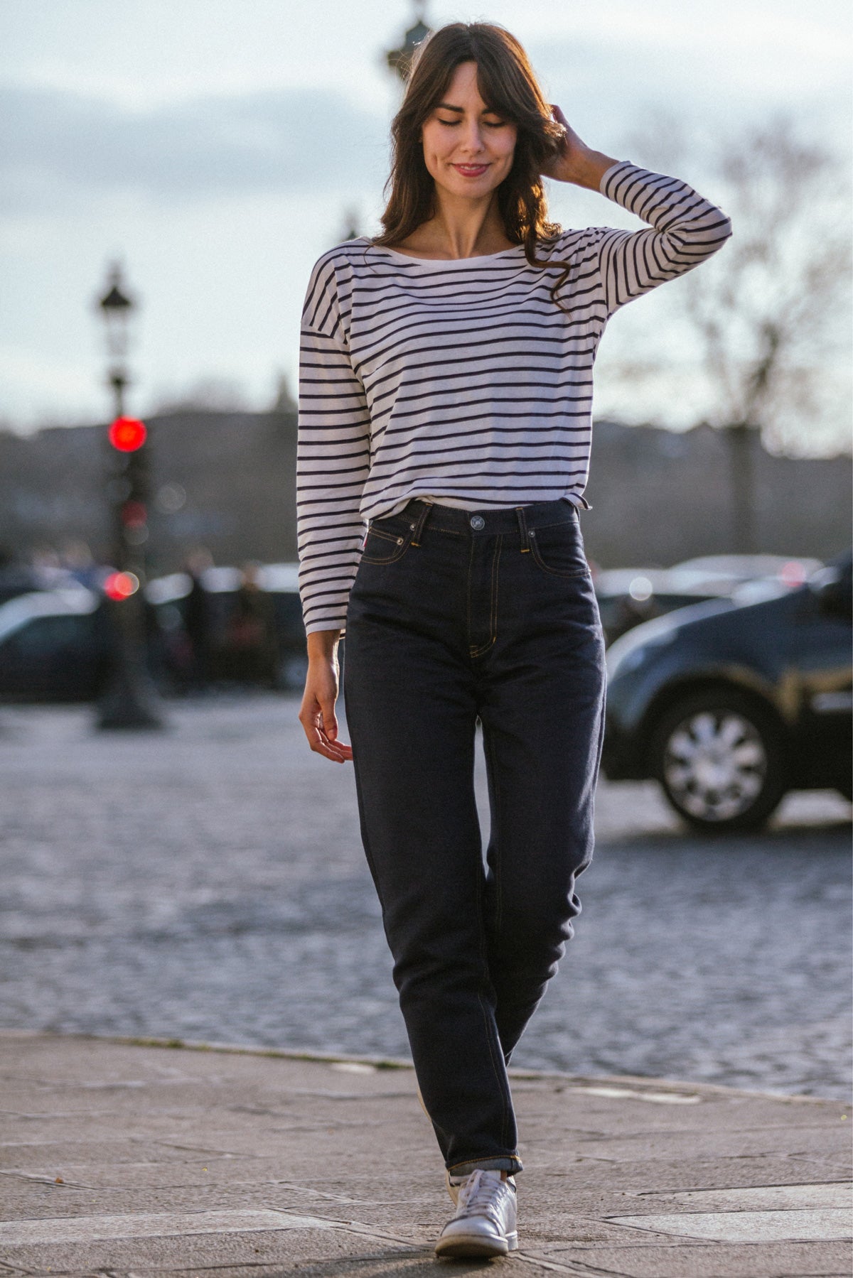 Modèle femme portant le jeans en chanvre et coton bio Isla pour femme, de couleur bleu avec coupe droite et taille haute, fermeture à glissière et liseré rouge distinctif sur le revers, en tissu sergé croisé sur fond urbain.