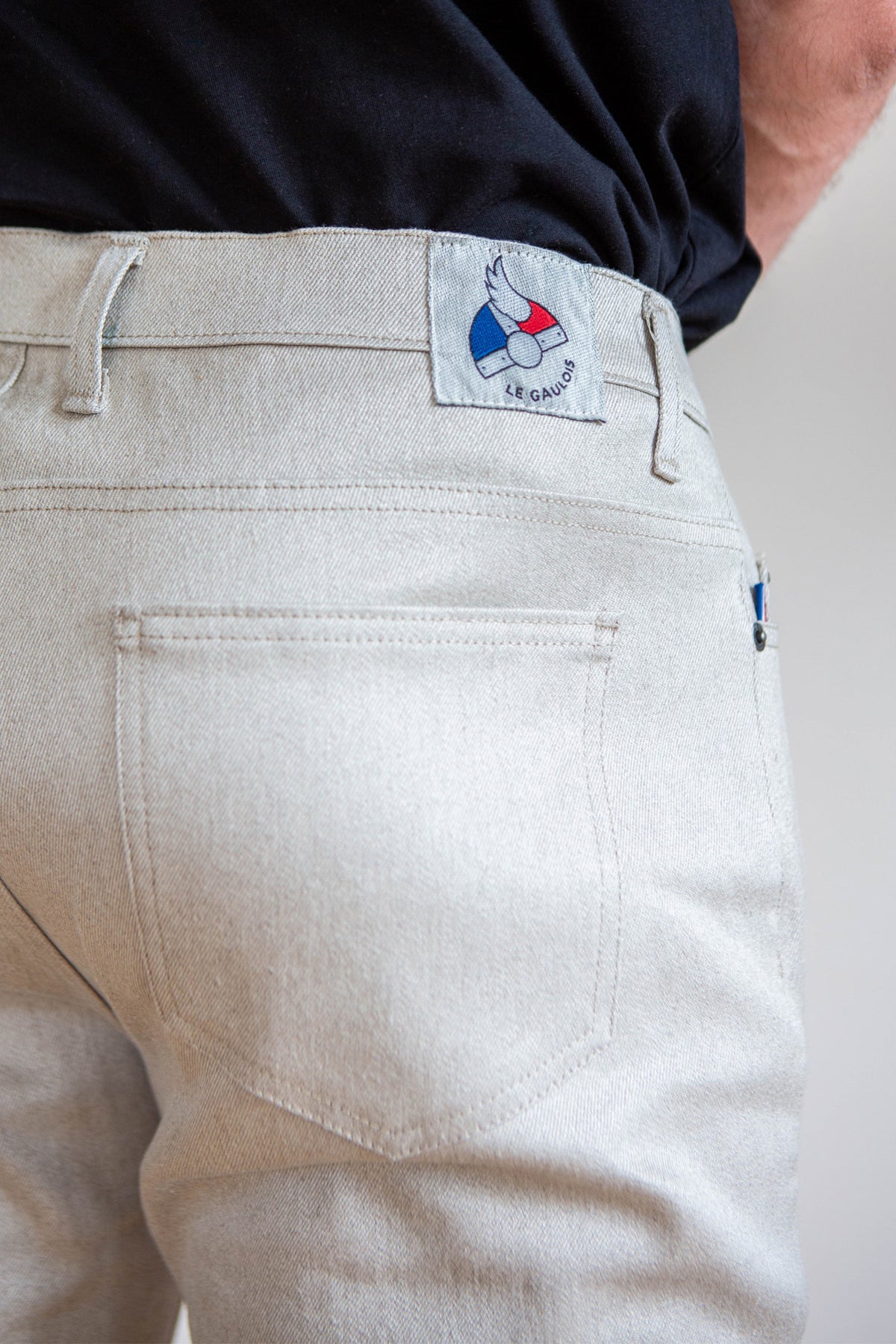 Jeans en lin Massalia en Lin Naturel à coupe droite présentant une couleur beige clair ivoire, non teinté, avec tissage sergé croisé, détail étiquette Le Gaulois sur la poche arrière sur une personne portant un haut noir, fabriqué en France - Le Gaulois Jeans