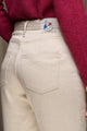 Plan rapproché sur le jeans en lin et laine mérinos Boutae Naturel pour femme avec une coupe droite et taille haute, couleur lin naturel, détail de la poche arrière et étiquette de la marque Le Gaulois jeans, porté avec un pull bordeaux, sur fond neutre