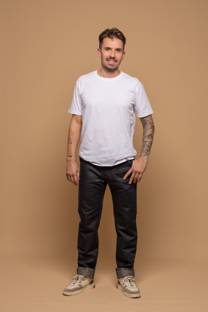 Modèle homme portant le jeans en lin et coton bio Cargus à coupe droite cargo et taille mi-haute, de couleur bleu jeans, avec un t-shirt blanc et des baskets beiges, sur fond neutre - Le Gaulois jeans