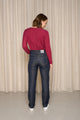 Modèle féminin de dos présentant le jeans en lin Condate Bleu en coupe droite et taille mi-haute, avec surpiqûres contrastées et fermeture à glissière, porté avec un pull bordeaux et des baskets blanches, sur un fond de rideau beige - Le Gaulois jeans