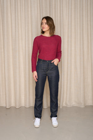 Femme présentant le pantalon Condate Bleu de catégorie pantalon, un jeans en lin 100% avec une coupe droite, taille mi-haute, couleur bleu jeans, finition glissière, porté avec un pull bordeaux et baskets blanches, sur un fond de rideau beige - Le Gaulois Jeans