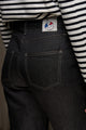 Modèle féminin présentant le jeans en lin Condate Noir avec coupe droite et taille mi-haute, détail de la poche arrière et du patch Le Gaulois, sur un haut à rayures noires et blanches - Le Gaulois jeans