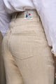 Vue arrière du jeans en chanvre Constance en chanvre naturel pour femme avec coupe droite, taille mi-haute et poches plaquées à l'arrière , présentant un bouton en bois de buis et une fermeture éclair recyclée, couleur naturelle, porté avec une chemise blanche ample, sur fond neutre.