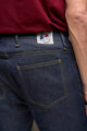 Gros plan sur le jeans en lin et élasthanne recyclé modèle Divio bleu pour homme avec une coupe près du corps et taille haute, montrant des détails de la poche arrière et de l'étiquette Le Gaulois, sur le fond d'un t-shirt bordeaux.