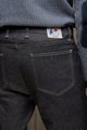 Vue rapprochée du jeans en lin et élasthanne recyclé modèle Divio Noir pour homme avec coupe près du corps et taille haute, présentant une poche arrière et l'étiquette Le Gaulois sur un tissu noir jeans, sur fond flou - Le Gaulois jeans
