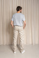 Homme de dos portant le pantalon Lugdunum en lin naturel avec coupe chino, taille haute et légèrement effilé aux chevilles, couleur ivoire sans teinture, accompagné d'un t-shirt gris et de baskets blanches, sur fond neutre - Le Gaulois jeans en lin