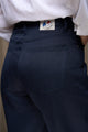 Vue arrière d'une femme portant le jeans en lin Lutèce Bleu couleur bleu marine avec une coupe Mom confortable sur les hanches et étroit aux chevilles, taille haute et fermeture à glissière, mettant en avant la qualité du tissu sergé croisé en lin de Normandie et l'étiquette Le Gaulois jeans, sur un fond uni.