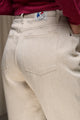 Jeans en lin Lutèce en Lin Naturel avec coupe Mom, taille haute et couleur ivoire naturel sans teinture, tissé en sergé croisé 100% lin de Normandie, présenté avec une étiquette Le Gaulois sur la poche arrière et un pull bordeaux, mettant en avant la qualité et le confort du pantalon - Le Gaulois jeans