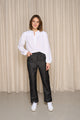 Modèle femme présentant le jeans en lin Lutèce Noir de coupe Mom taille haute, confortable sur les hanches et étroite aux chevilles, couleur noire, porté avec une chemise blanche et des baskets blanches, sur un fond de rideau beige - Le Gaulois Jeans