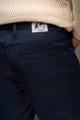 Plan rapproché du jeans en lin Massalia Bleu pour homme par Le Gaulois jeans, couleur bleu marine, avec une coupe droite et taille mi-haute, affichant un tissage de sergé croisé et une étiquette de marque visible au niveau de la ceinture, porté sous un pull beige - fabriqué en France avec lin de Normandie.
