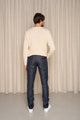 Homme de dos portant le jeans en lin Massalia Bleu à coupe droite, couleur bleu jeans, avec un pull crème et des baskets blanches, sur fond de rideau beige - Le Gaulois jeans