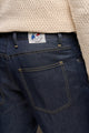 Modèle homme portant le jeans en lin Massalia Bleu à coupe droite, couleur bleu marine avec des surpiqûres jaunes, taille mi-haute légèrement effilée aux chevilles et fermeture à bouton, agrémenté d'un pull en maille crème, confectionné en France - Le Gaulois jeans
