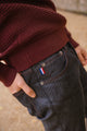 Plan rapproché sur le jeans en lin et laine mérinos Narbo Bleu avec coupe droite, montrant un léger effilage aux chevilles et une fermeture à bouton en métal, agrémenté d'un petit drapeau français sur la poche avant, le tout associé à un pull bordeaux - Le Gaulois jeans