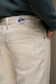 Jeans en lin et laine Narbo Naturel coupe droite avec finitions effilées aux chevilles, teinte lin naturel, bouton en métal et étiquette Le Gaulois sur la poche arrière, porté avec un haut en maille gris.
