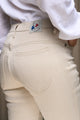 Modèle présentant le jeans en lin Nicia en Lin Naturel à taille haute et coupe près du corps en tissu sergé croisé, couleur naturelle ivoire sans teinture, avec fermeture à glissière et étiquette de marque Le Gaulois sur fond urbain neutre - Le Gaulois Jeans