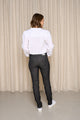Modèle femme de dos portant le jeans en lin et élasthanne recyclé Nicia Noir à coupe près du corps, taille haute et couleur noir jeans, assorti d'une chemise blanche et de baskets blanches, debout devant un rideau beige - Le Gaulois jeans