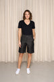 Modèle féminin présentant le bermuda Olbia 100% lin noir jeans à taille mi-haute et longueur genou, assorti d'un t-shirt noir et des baskets blanches, sur un fond de rideau beige - jeans en 100% lin