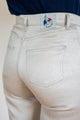 Modèle féminin de dos portant le jeans en lin Condate en Lin Naturel, couleur ivoire naturel sans teinture, avec une coupe droite et une taille mi-haute, détail d'un écusson Le Gaulois sur la poche arrière, confectionné en France avec un tissu 100% lin de Normandie.