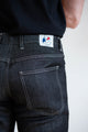 Homme portant le jeans en lin Massalia Noir à coupe droite légèrement effilée aux chevilles avec poches arrière visibles et étiquette Le Gaulois sur fond uni - Le Gaulois Jeans