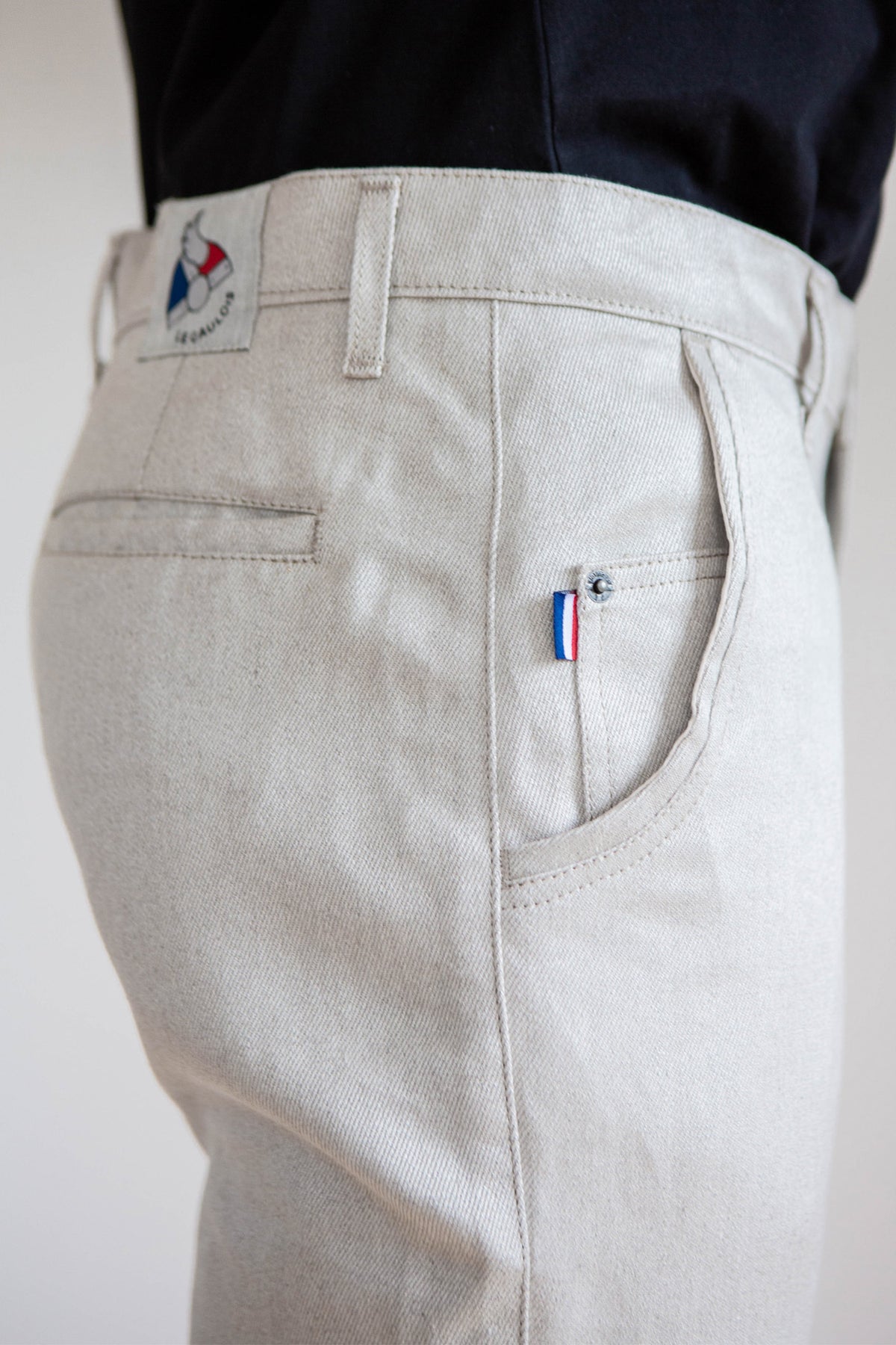 Jeans en lin Lugdunum en Lin Naturel de couleur beige clair ivoire, coupe chino confortable avec taille haute et légèrement effilé aux chevilles, doté d'une fermeture à glissière, fabriqué en France, 100% Lin de Normandie sans teinture, visible de profil avec détail de la poche arrière et étiquette tricolore - Le Gaulois jeans