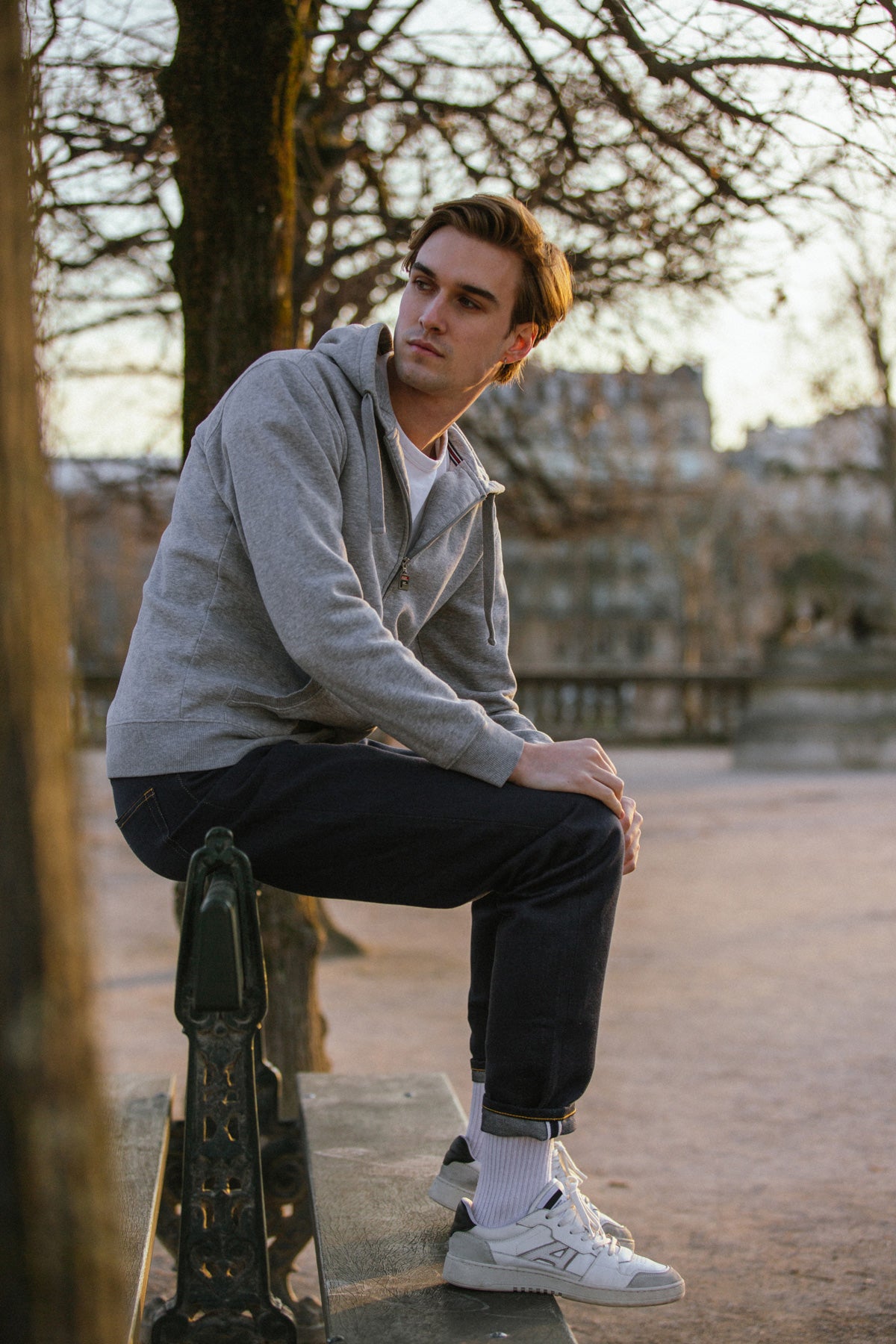 Homme portant le jeans en chanvre et coton bio Isla pour homme, de couleur bleue à coupe droite et taille haute, avec fermeture à glissière et liseré rouge sur le revers, combiné à un sweat gris et des baskets blanches, posant à l'extérieur sur un banc - Le Gaulois jeans